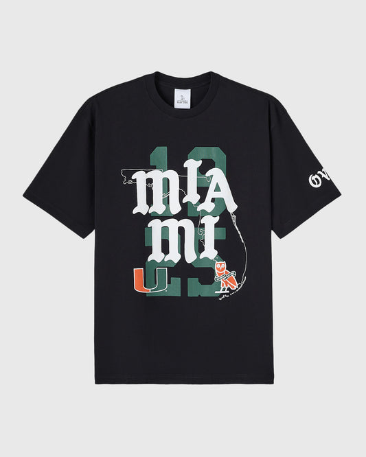 Black t-shirt with white "UM" text overlay on green Florida state map, featuring University of Miami logo and mascot graphic.
