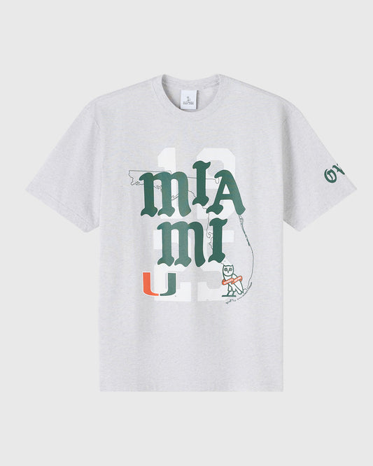 Ash heather grey t-shirt with University of Miami "U" logo, "mIA" text, and mascot graphic in green and orange.