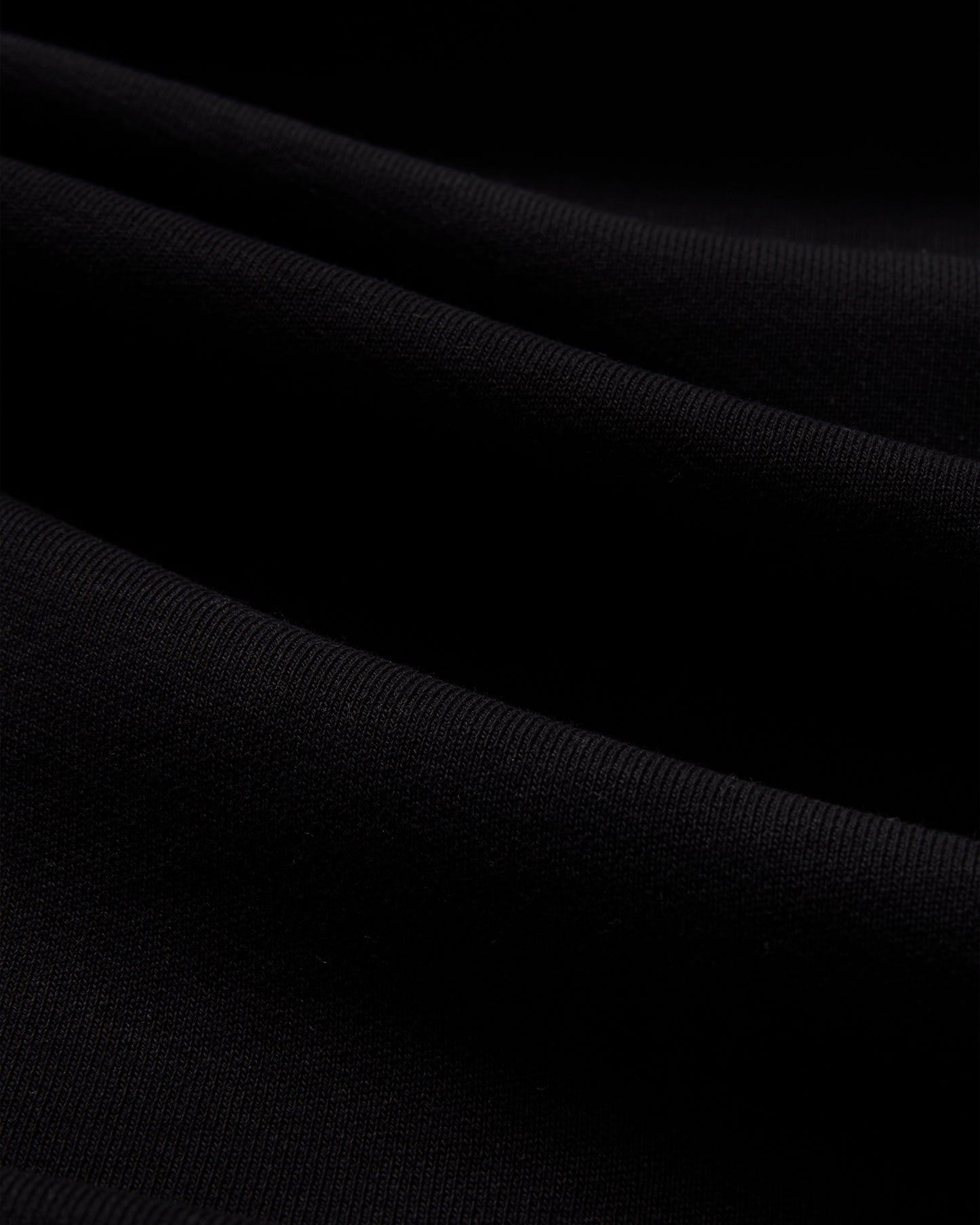 Black crewneck sweatshirt fabric with ribbed knit texture and diagonal folds.