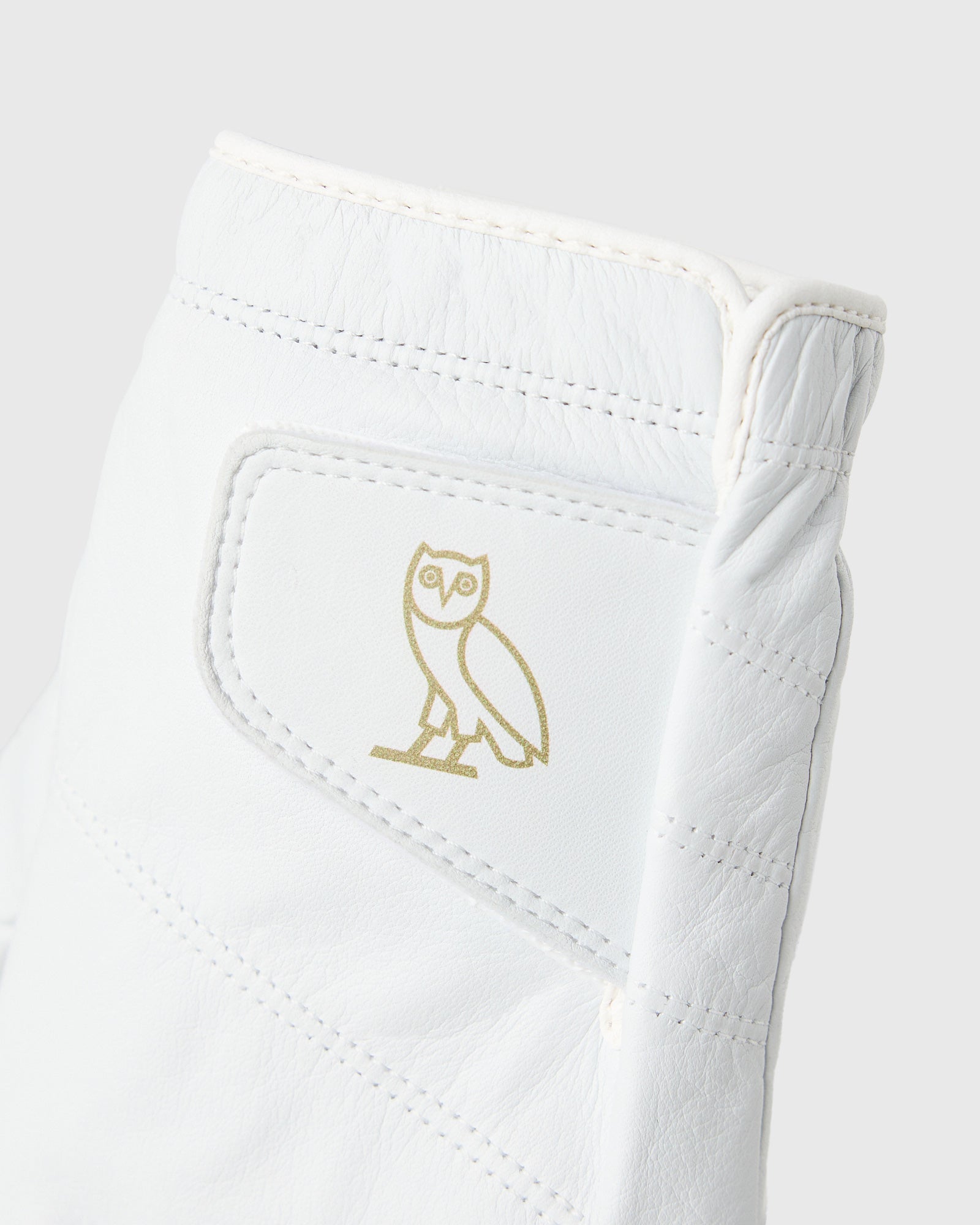 White golf glove with gold owl logo and stitched details on palm and back.