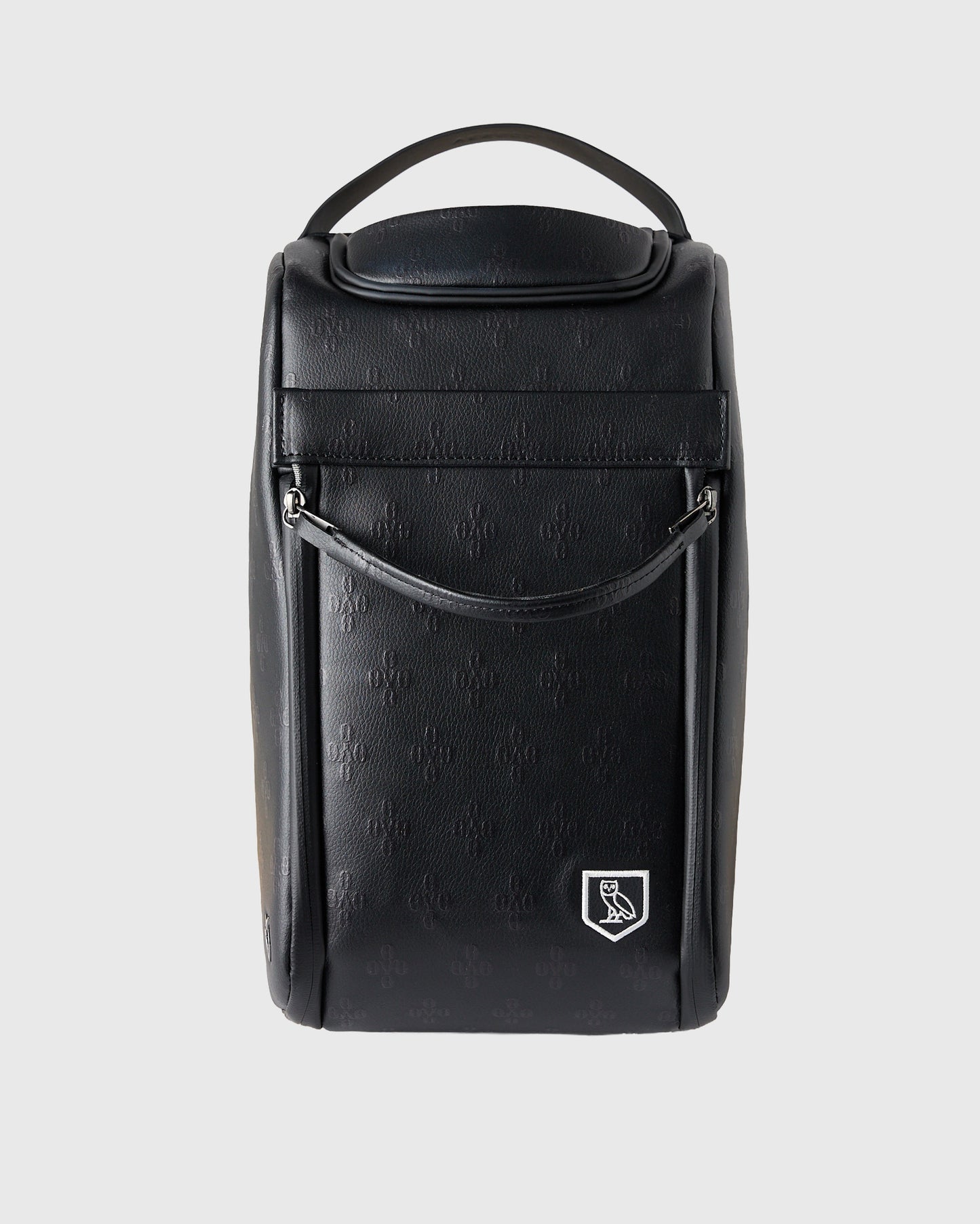 Black cylindrical golf shoe bag with handle, monogram texture, and crest logo on front.