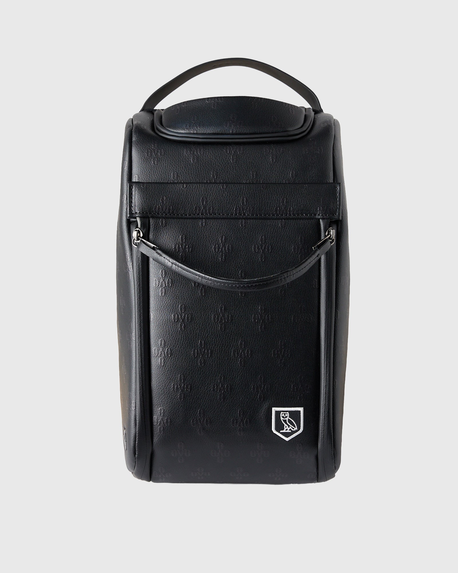 Black cylindrical golf shoe bag with handle, monogram texture, and crest logo on front.