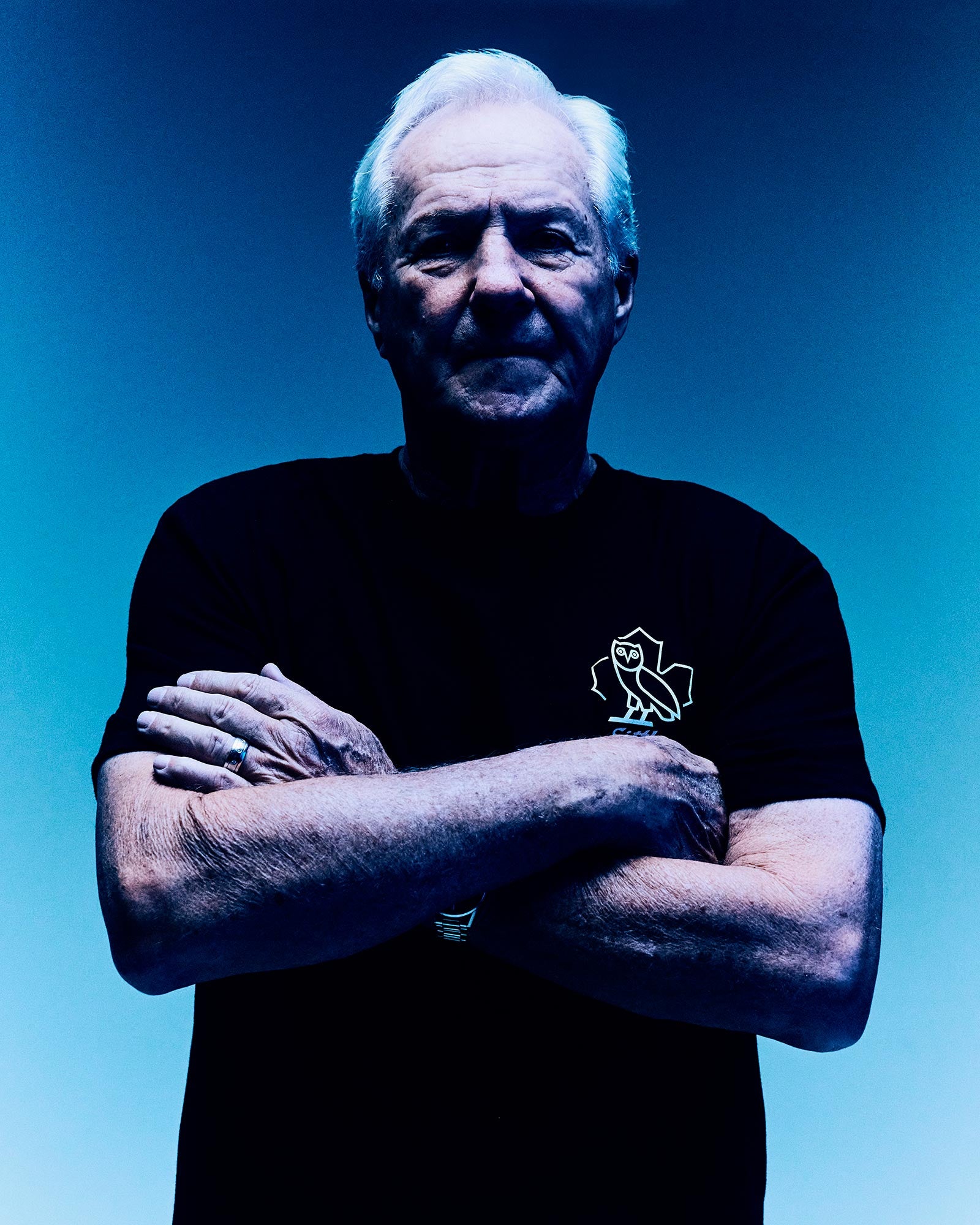 Darryl Sittler wearing a black October's Very Own t-shirt with a logo against a blue background