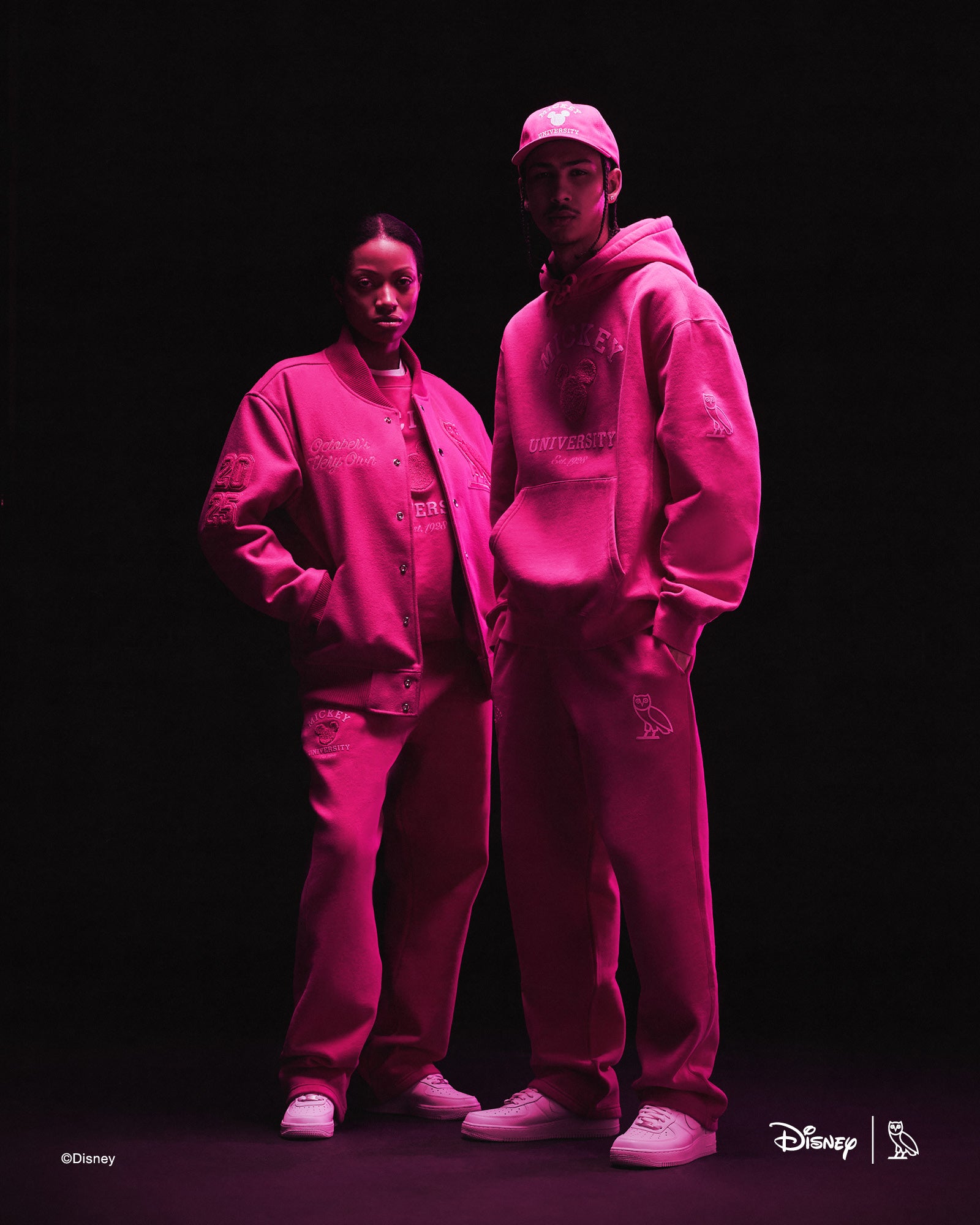 Two people wearing pink October's Very Own x Disney outfits with a dark background
