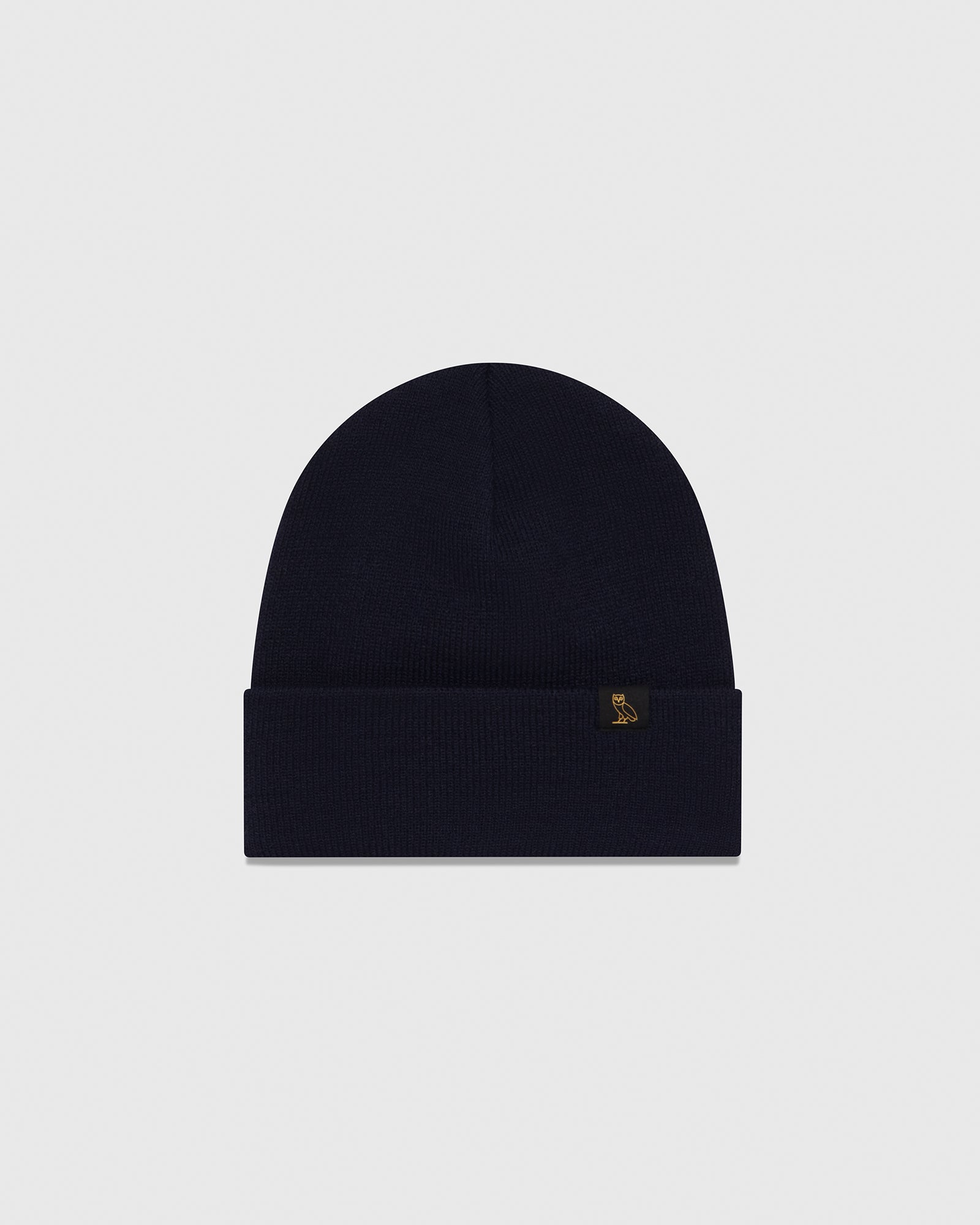 Navy ribbed knit beanie with small gold owl emblem on fold-over cuff.