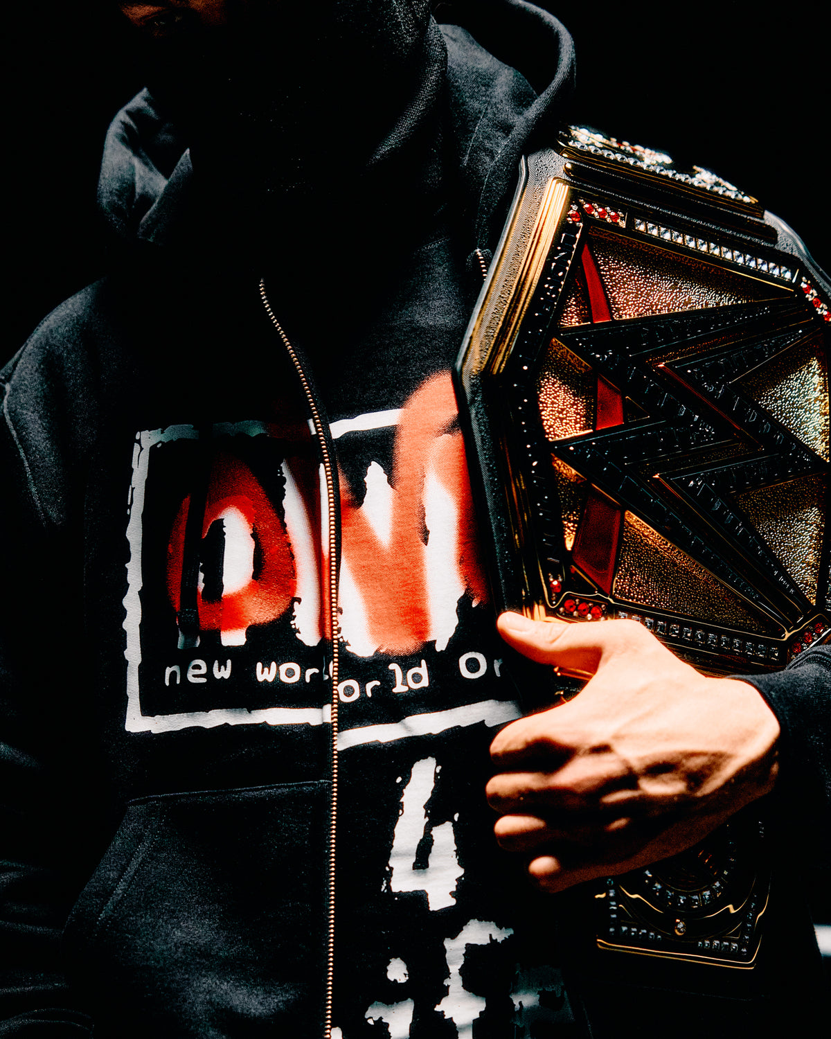 Person wearing a black hoodie with text, holding a wrestling championship belt. October's Very Own and WWE.