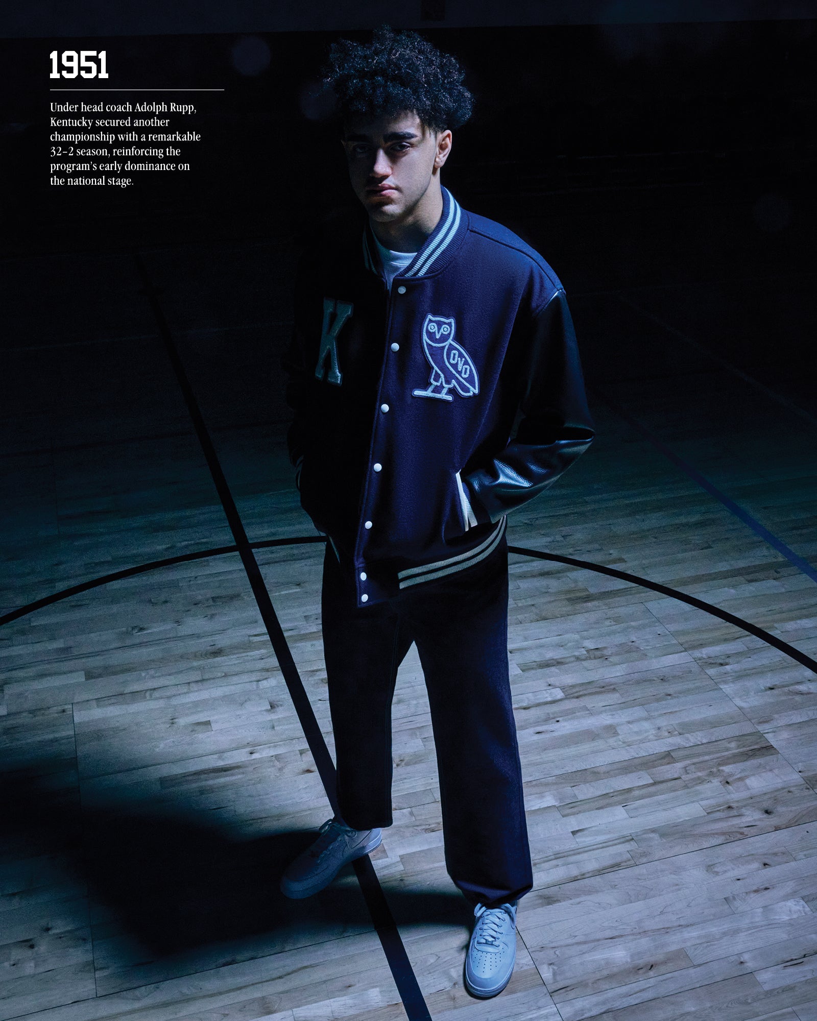 1951. Under head coach Adolph Rupp, Kentucky secured another championsihp with a remarkable 32.2 season, reinforcing the program's early dominance on the national stage. Person wearing a October's Very Own x Kentucky Wildcats varsity jacket, stand on a basketball court.