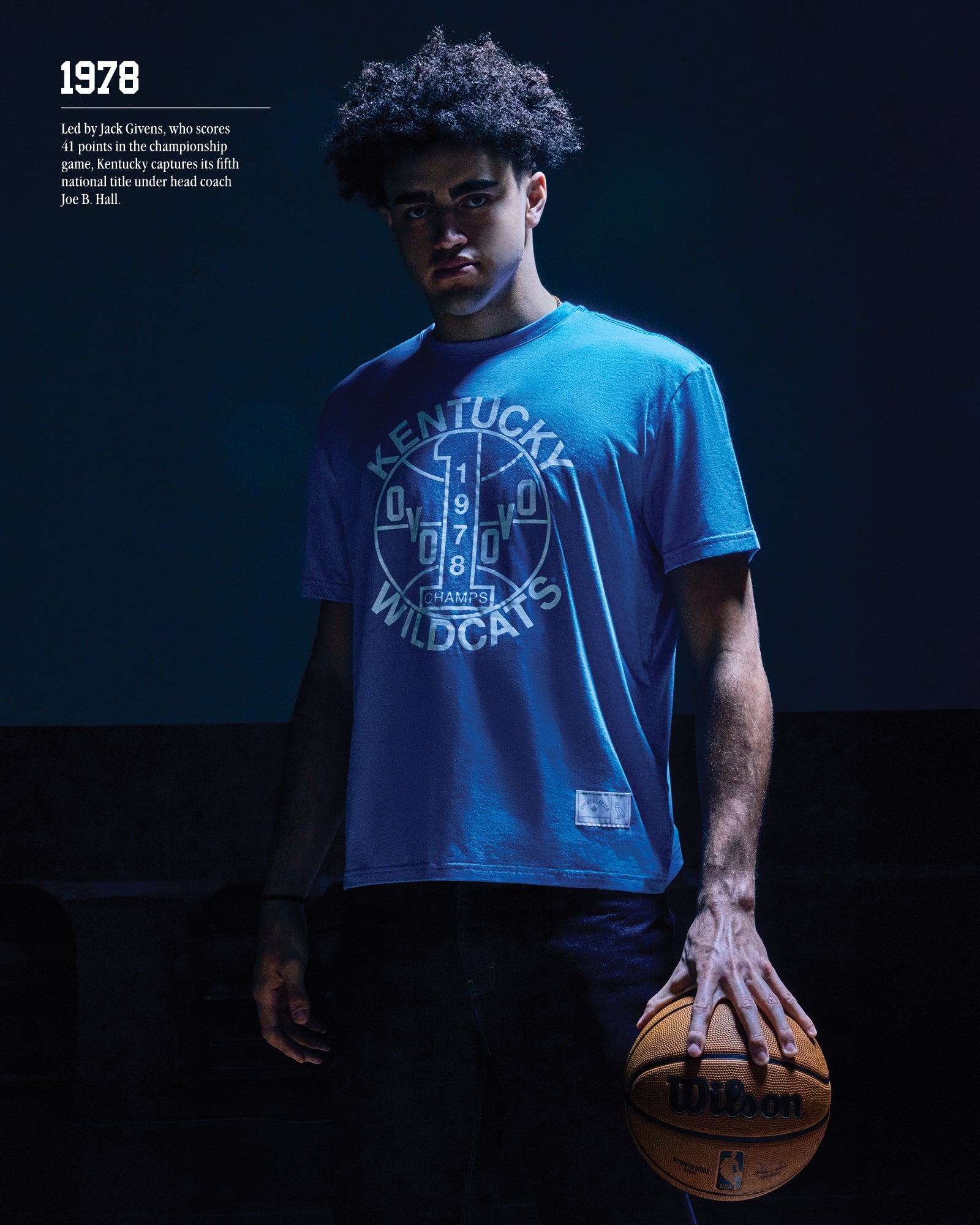 1978. Led by Jack Givens, who scores 41 points in the championship game, Kentucky captures its fifth national titlge under head couch Joe B. Hall.
Person wearing a blue October's Very Own x Kentucky Wildcats t-shirt holding a basketball against a dark background