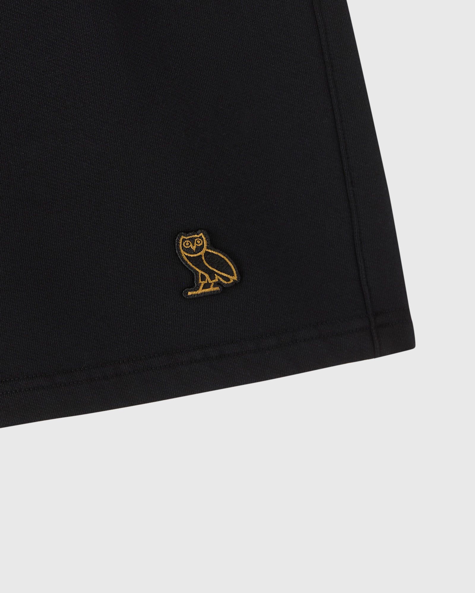 Black sweatshort with gold owl embroidery on thigh.