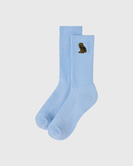 Pair of light blue ribbed crew socks with small black owl emblem on one sock.
