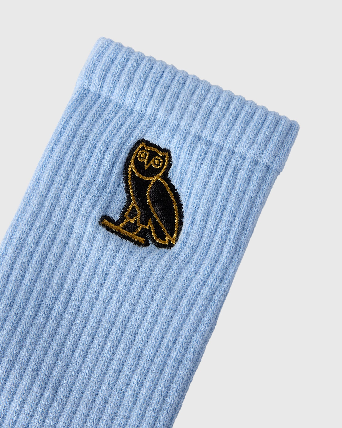 Light blue ribbed sock with black and gold embroidered owl patch.