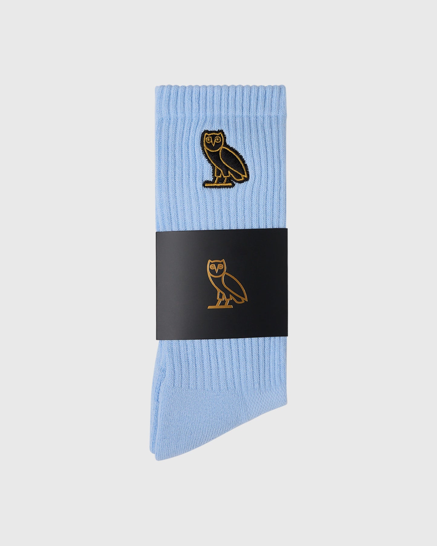 Light blue ribbed socks with gold owl embroidery on leg, displayed with black band wrapper.