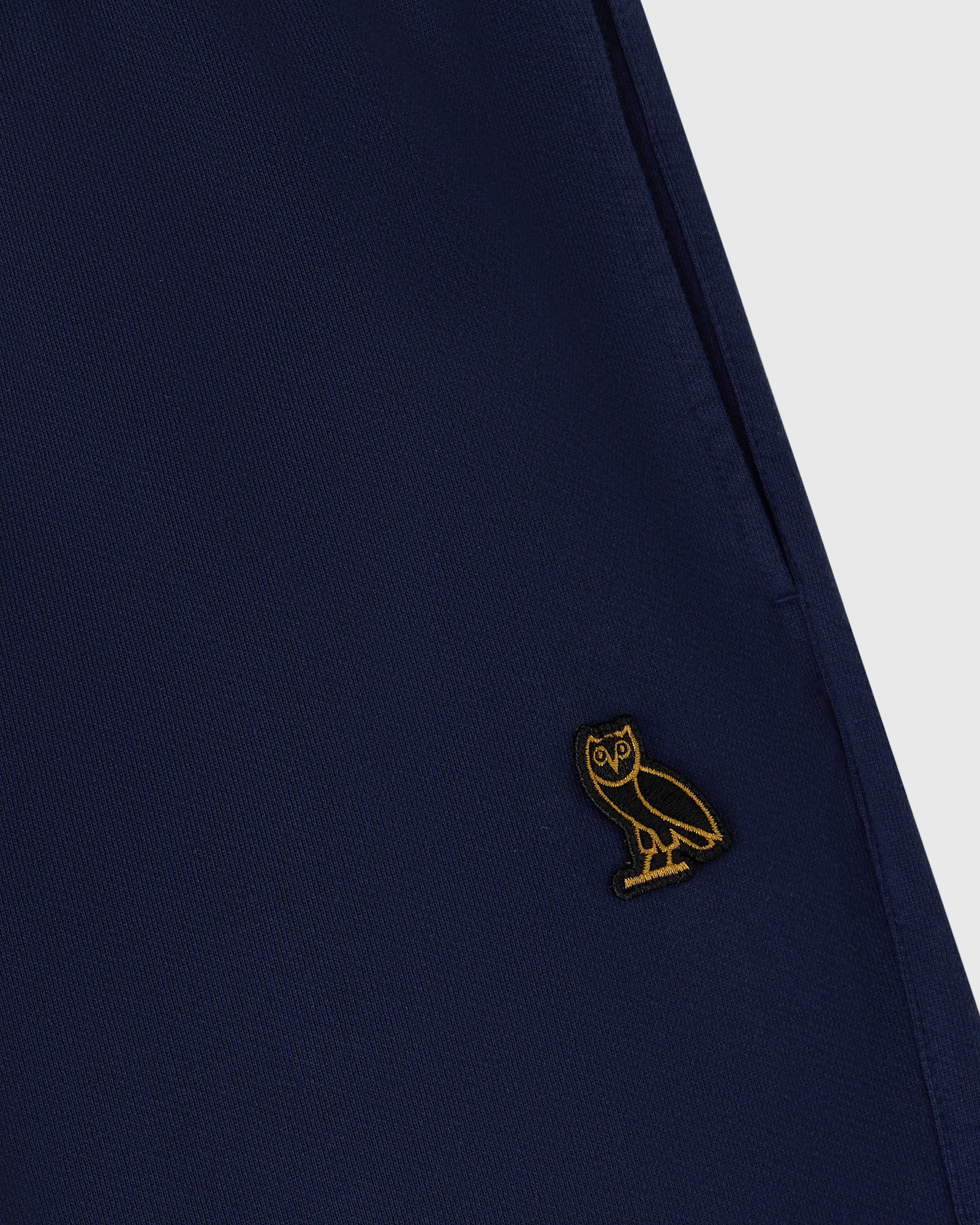 Navy sweatpants with ribbed texture and small gold owl embroidery on thigh.