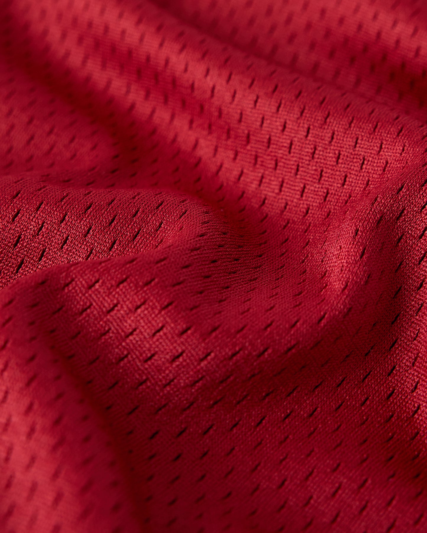 Deep red mesh fabric with small perforated holes throughout, showing texture and weave detail.