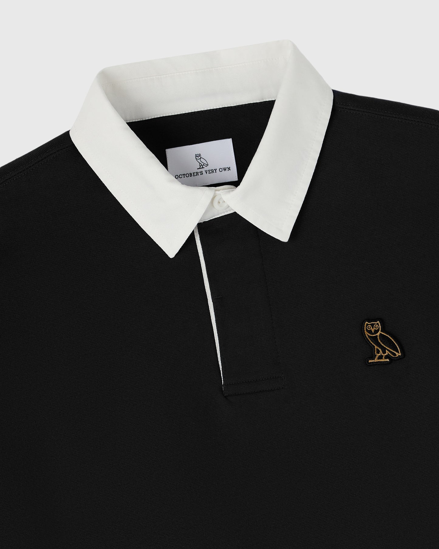 Black rugby polo with white collar and placket, gold owl embroidered on chest.