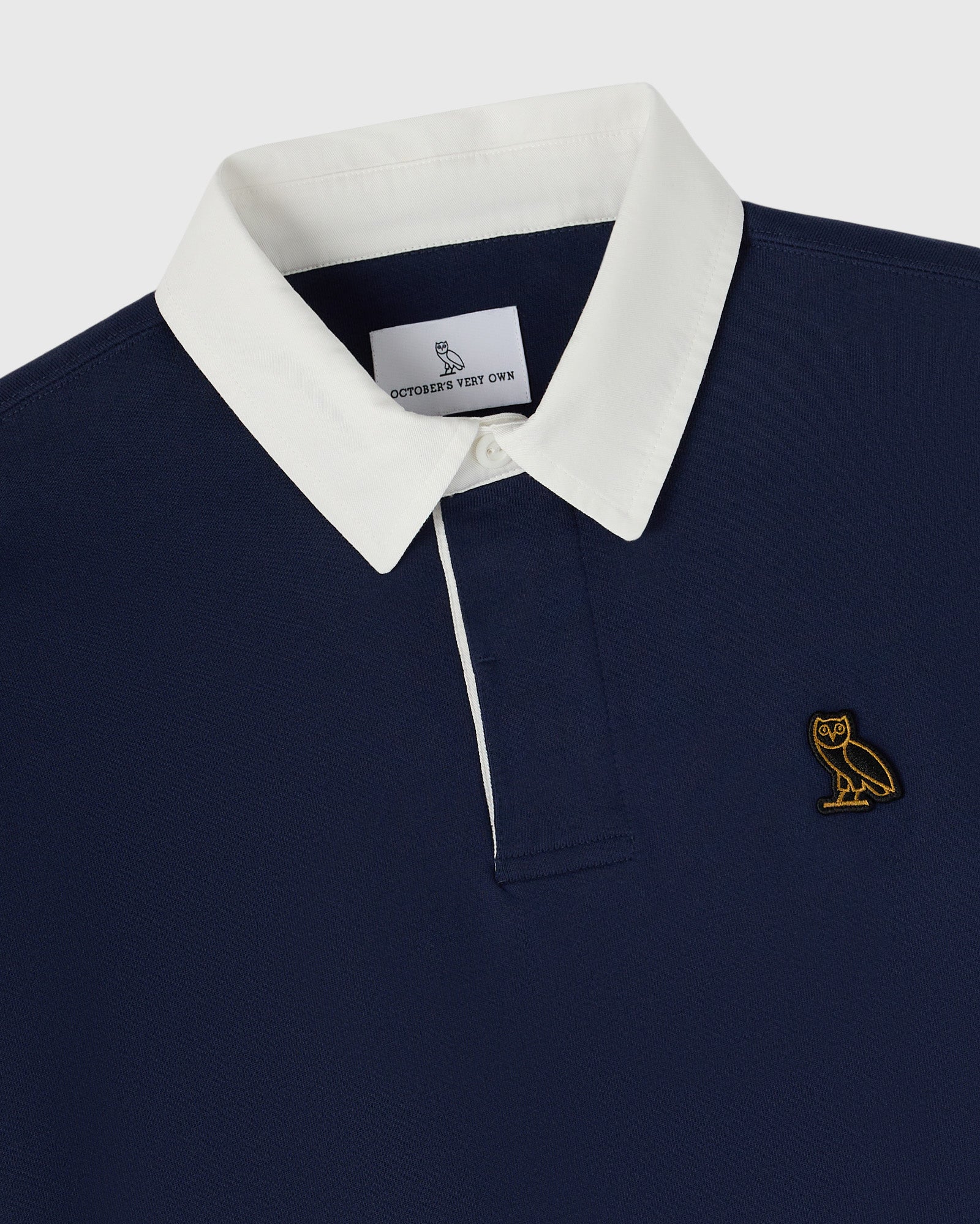 Navy rugby polo with white collar and gold owl embroidered logo on chest.