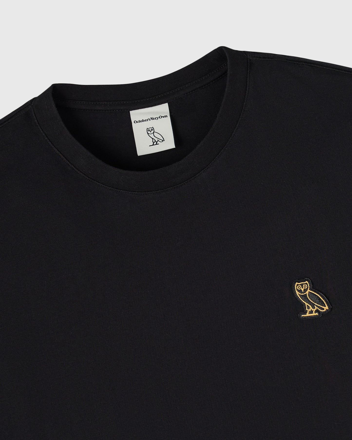 Black long-sleeve tee with crew neckline and small gold owl embroidery on chest.