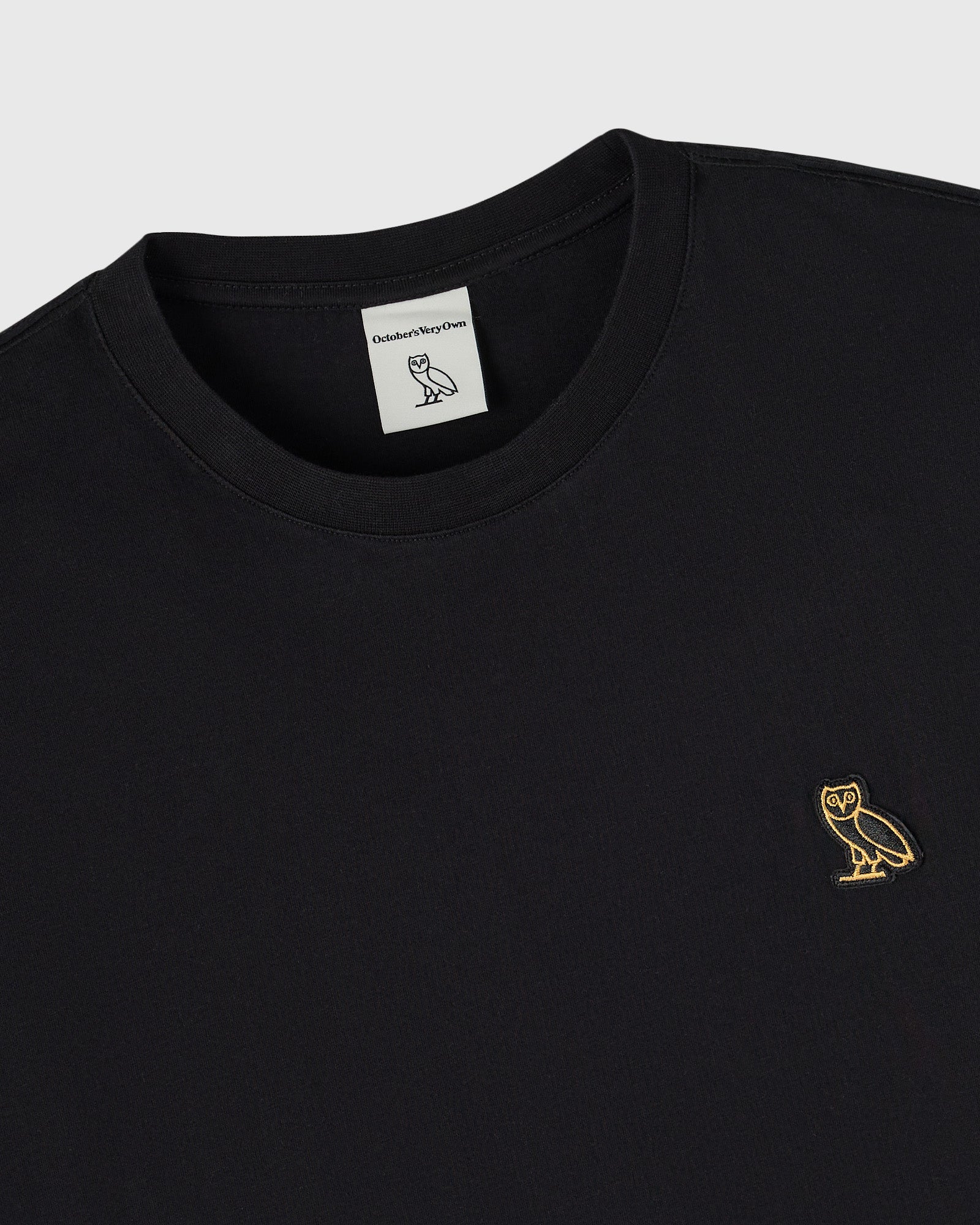 Black long-sleeve tee with crew neckline and small gold owl embroidery on chest.