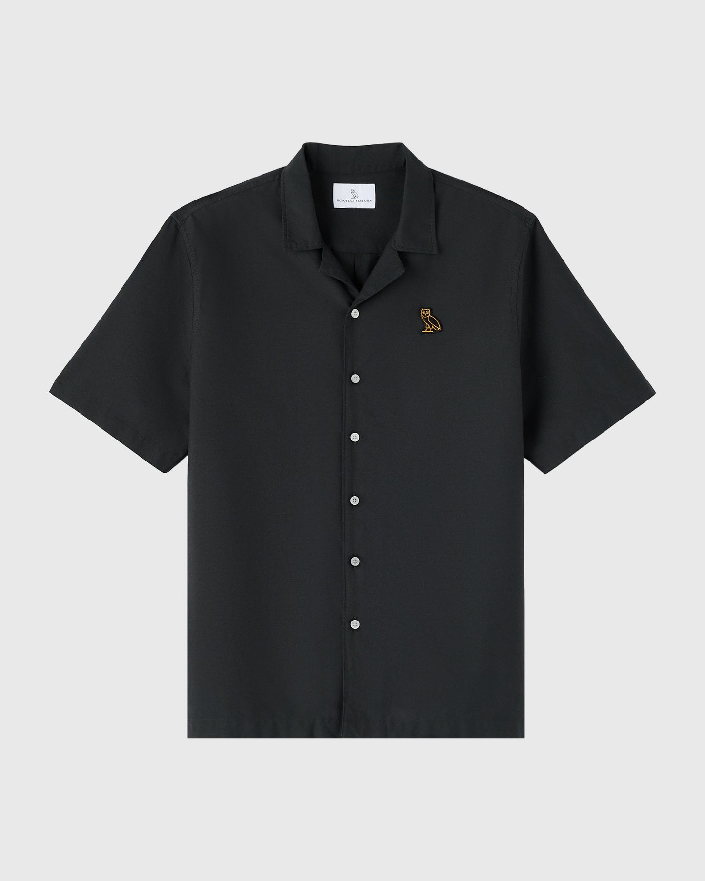 Black short-sleeve camp shirt with white buttons and small embroidered owl logo on chest.