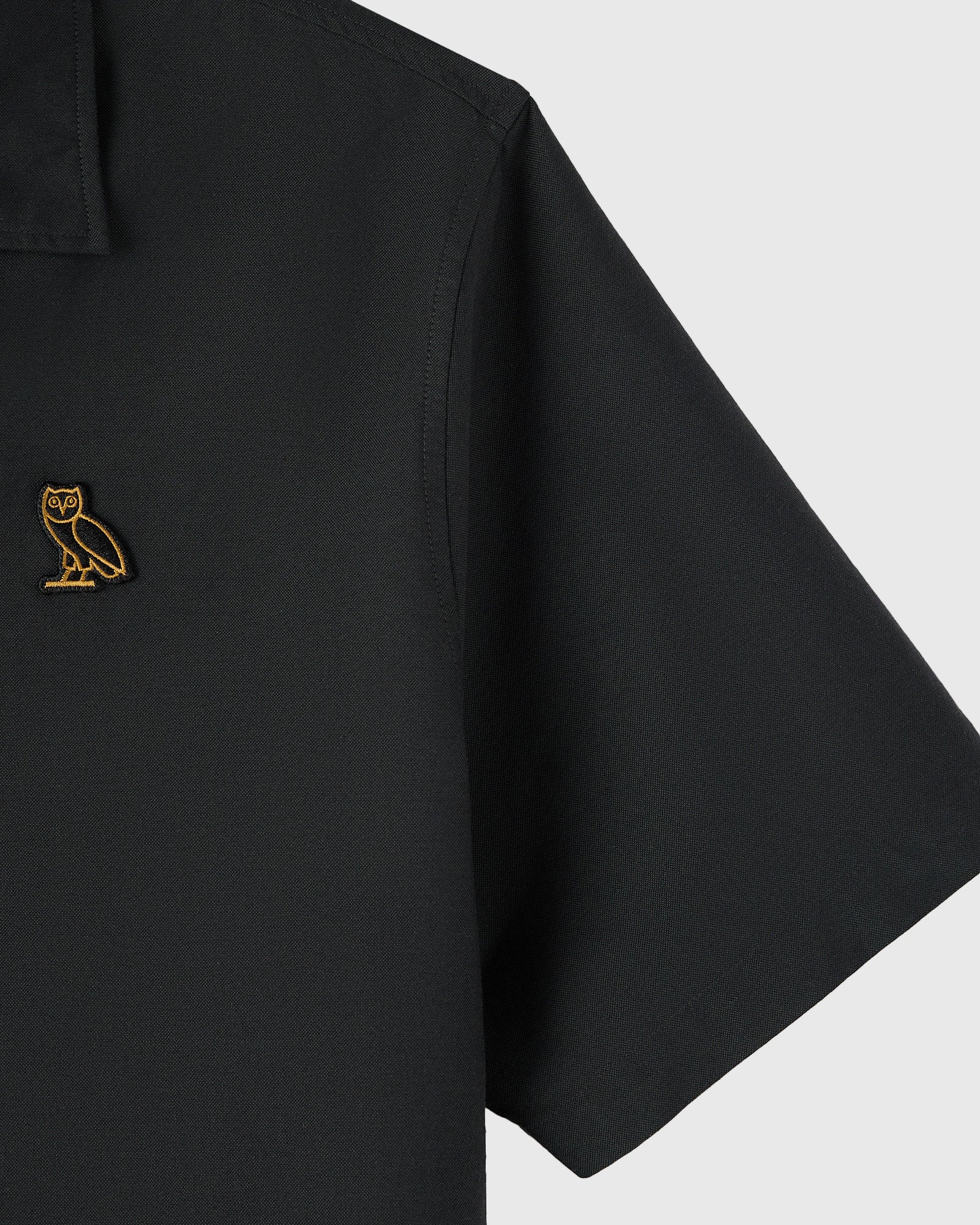 Black camp shirt with gold owl embroidery on chest pocket and short sleeves.