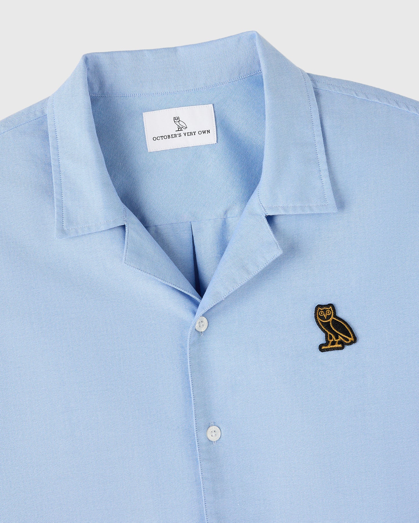 Light blue camp shirt with pointed collar, white buttons, and embroidered owl logo on chest.