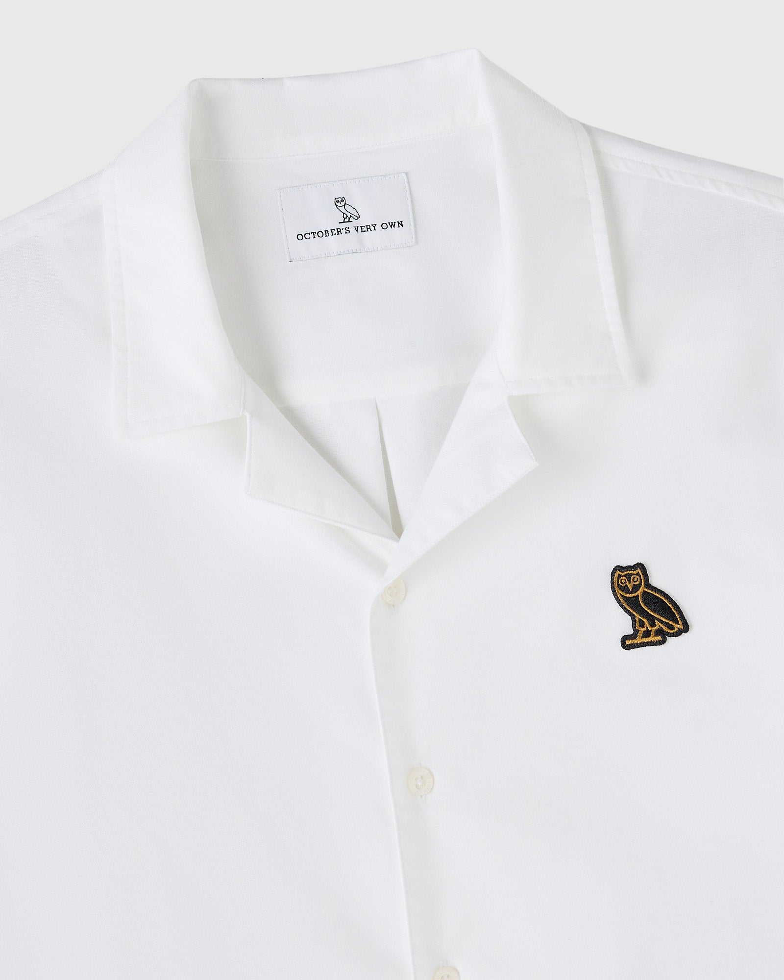 White oxford camp shirt with embroidered owl logo on chest and brand label on interior neckline.