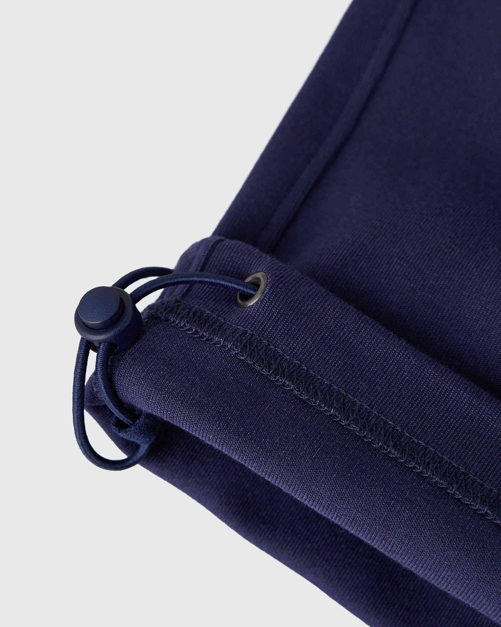 Dark navy sweatpant waistband with drawstring and metal eyelets, close-up detail view.