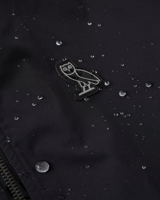 Black twill shell with owl logo and water beads demonstrating water-repellent fabric.