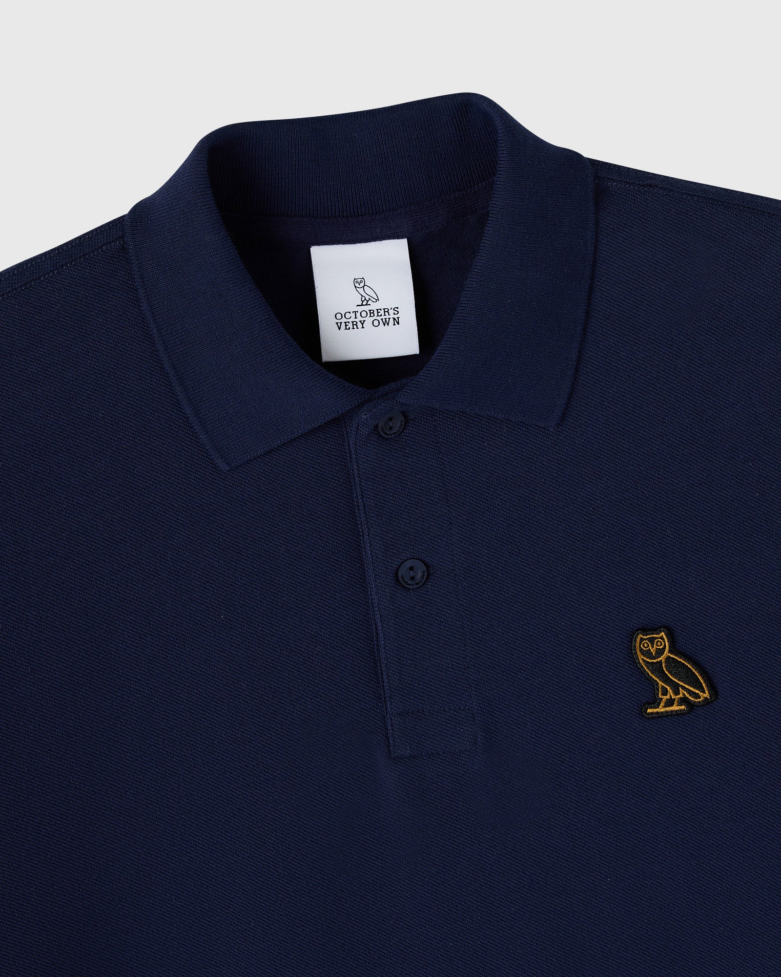 Navy polo shirt with ribbed collar, button front closure, and gold owl embroidered on chest.