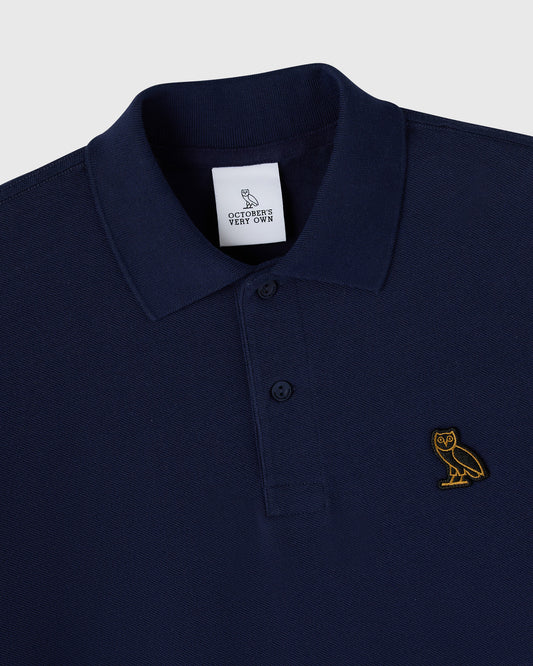 Navy polo shirt with ribbed collar, button front closure, and gold owl embroidered on chest.