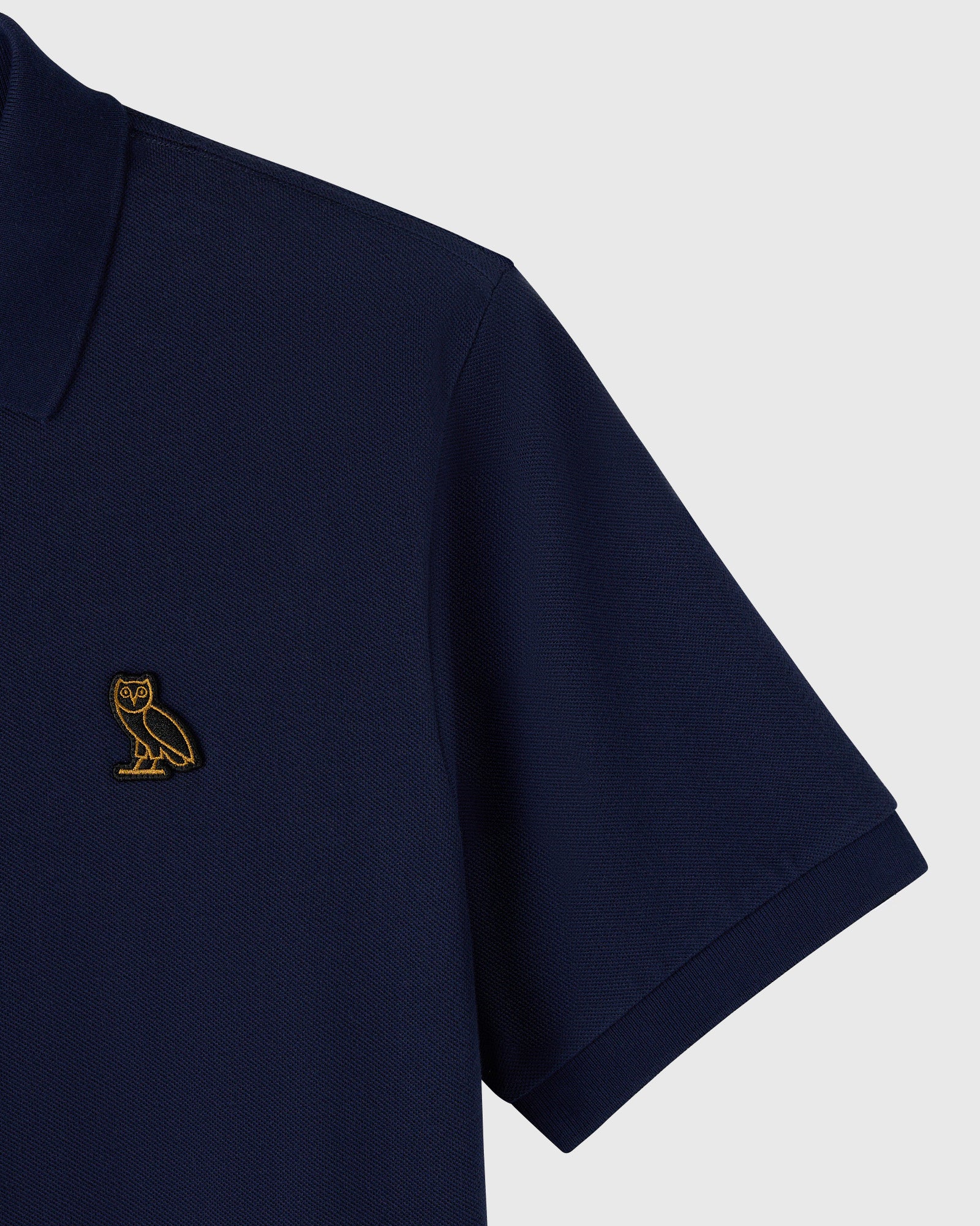 Navy polo shirt with small gold owl embroidered on chest and ribbed collar and sleeves.