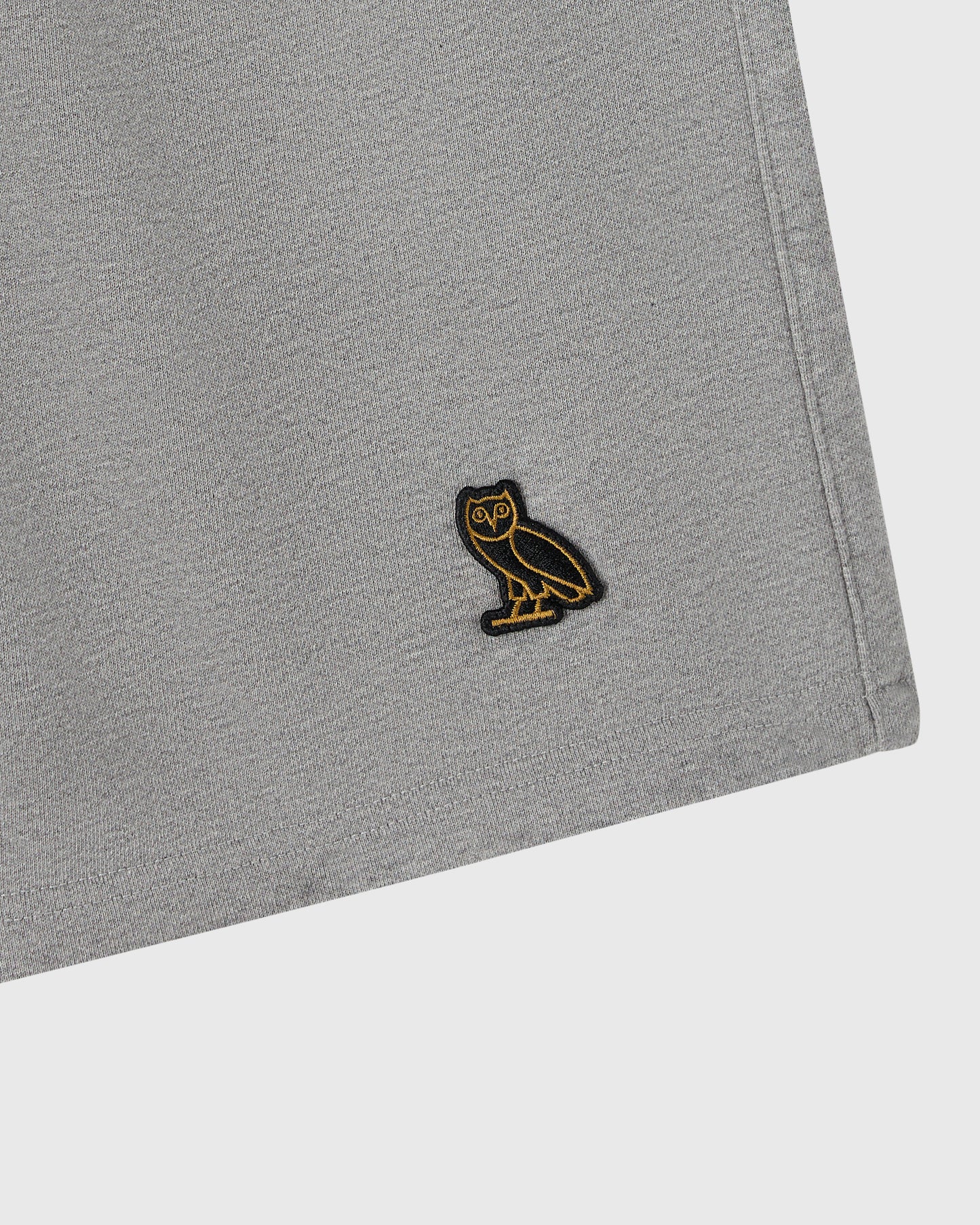 Heather grey sweatshort with small black and gold owl embroidered patch on thigh.