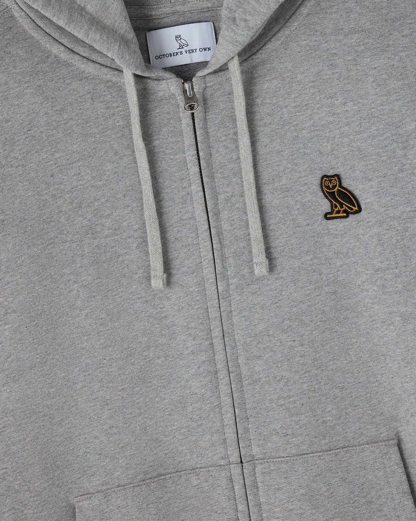 Heather grey full-zip hoodie with drawstrings, gold owl embroidery on chest, and brand label visible at neckline.