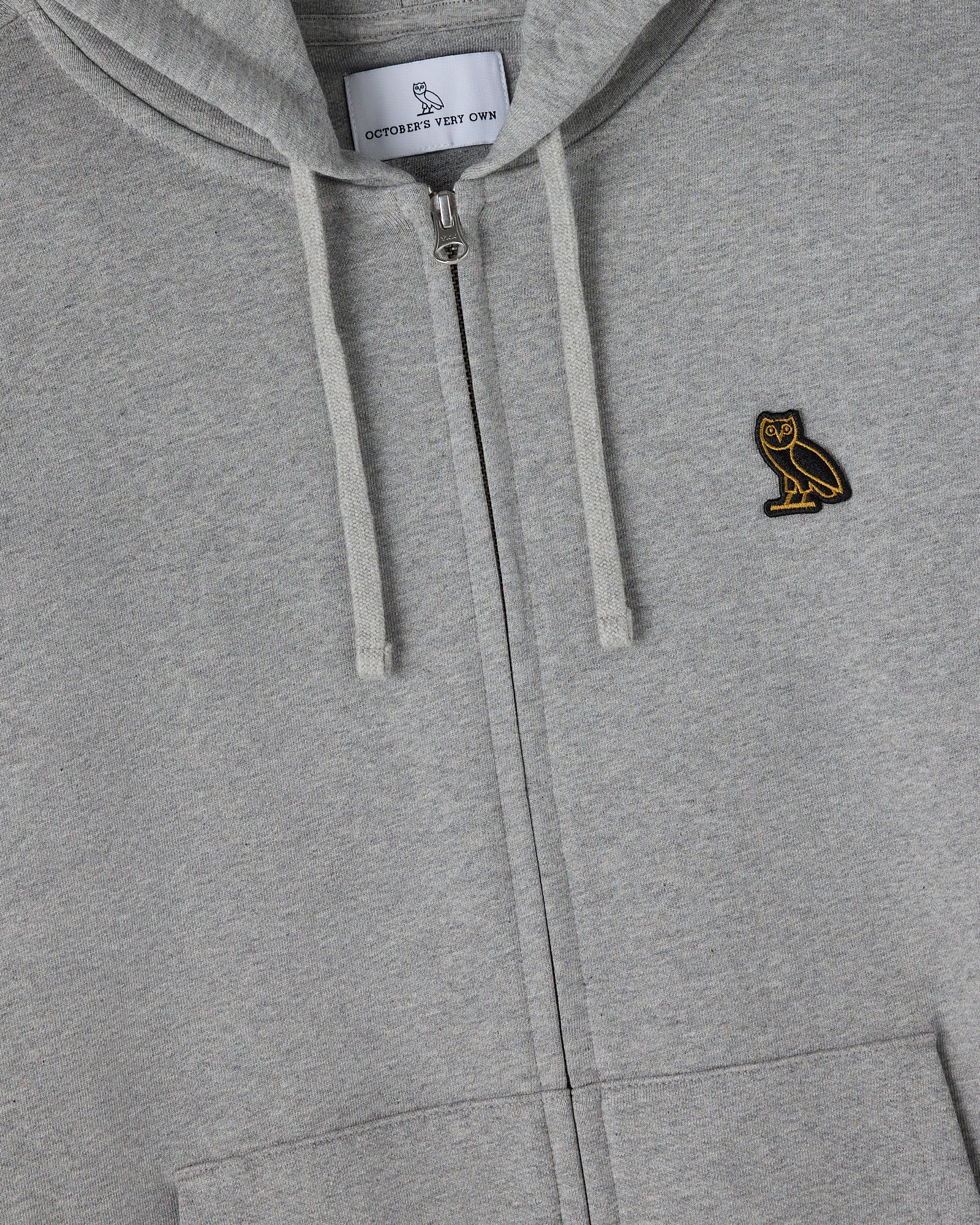 Heather grey full-zip hoodie with drawstrings, gold owl embroidery on chest, and brand label visible at neckline.