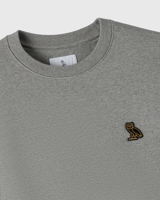 Heather grey crewneck sweatshirt with ribbed neckline and small owl embroidered patch on chest.