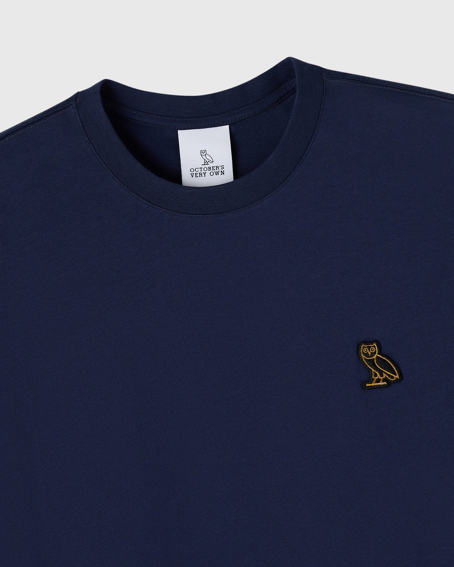 Navy crew neck t-shirt with small gold owl embroidery on chest and brand label at neckline.