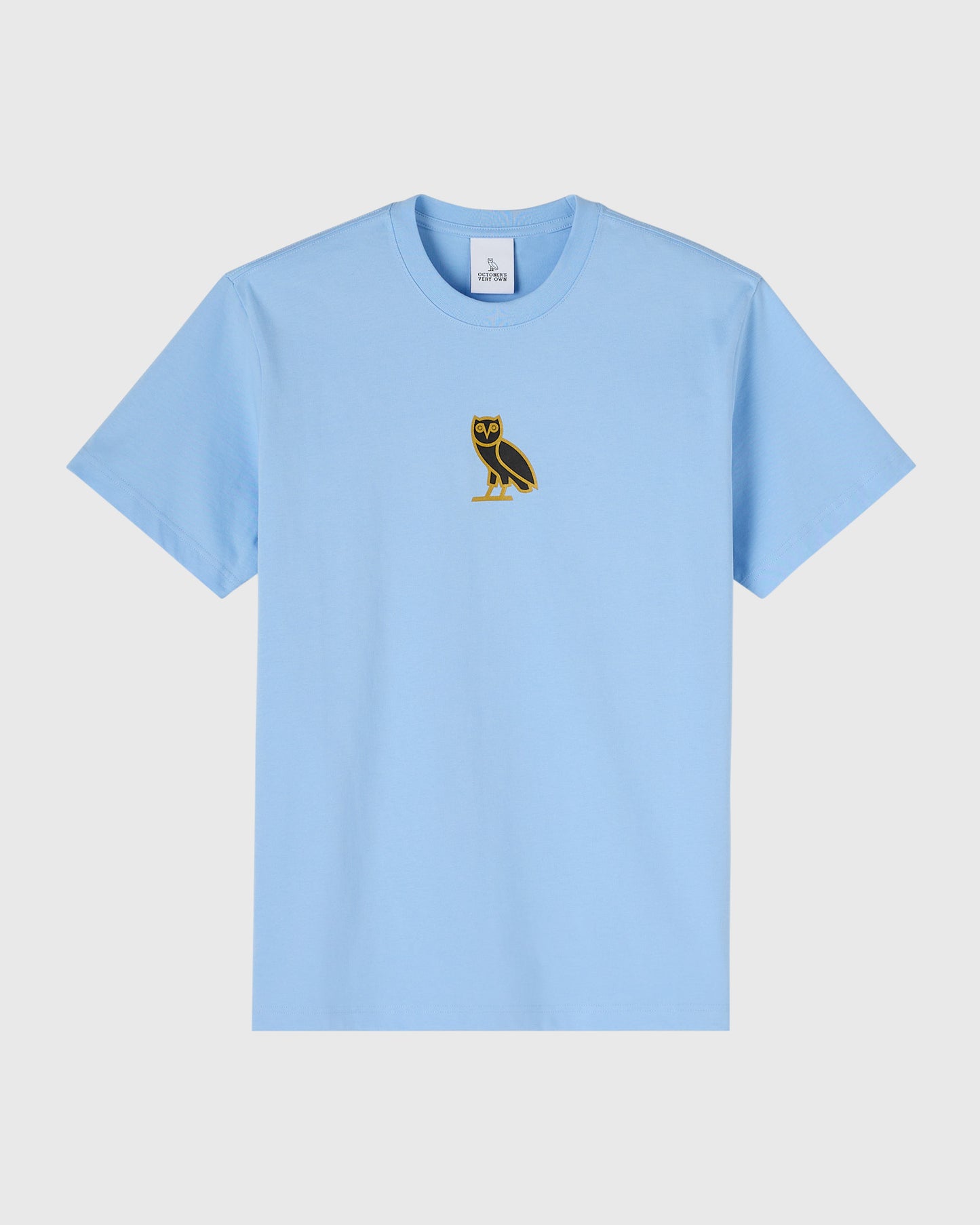 Light blue t-shirt with small black and gold owl emblem on chest.