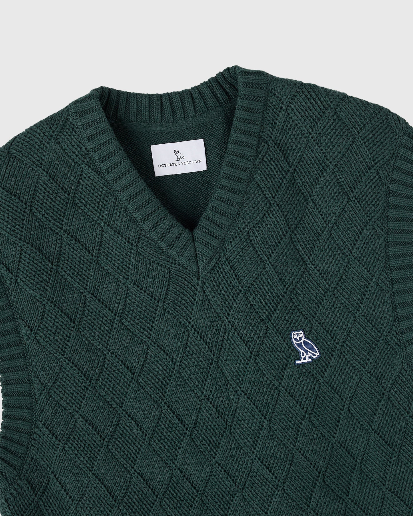 Midnight green basketweave sweater vest with V-neckline, ribbed collar and armholes, and embroidered owl logo.