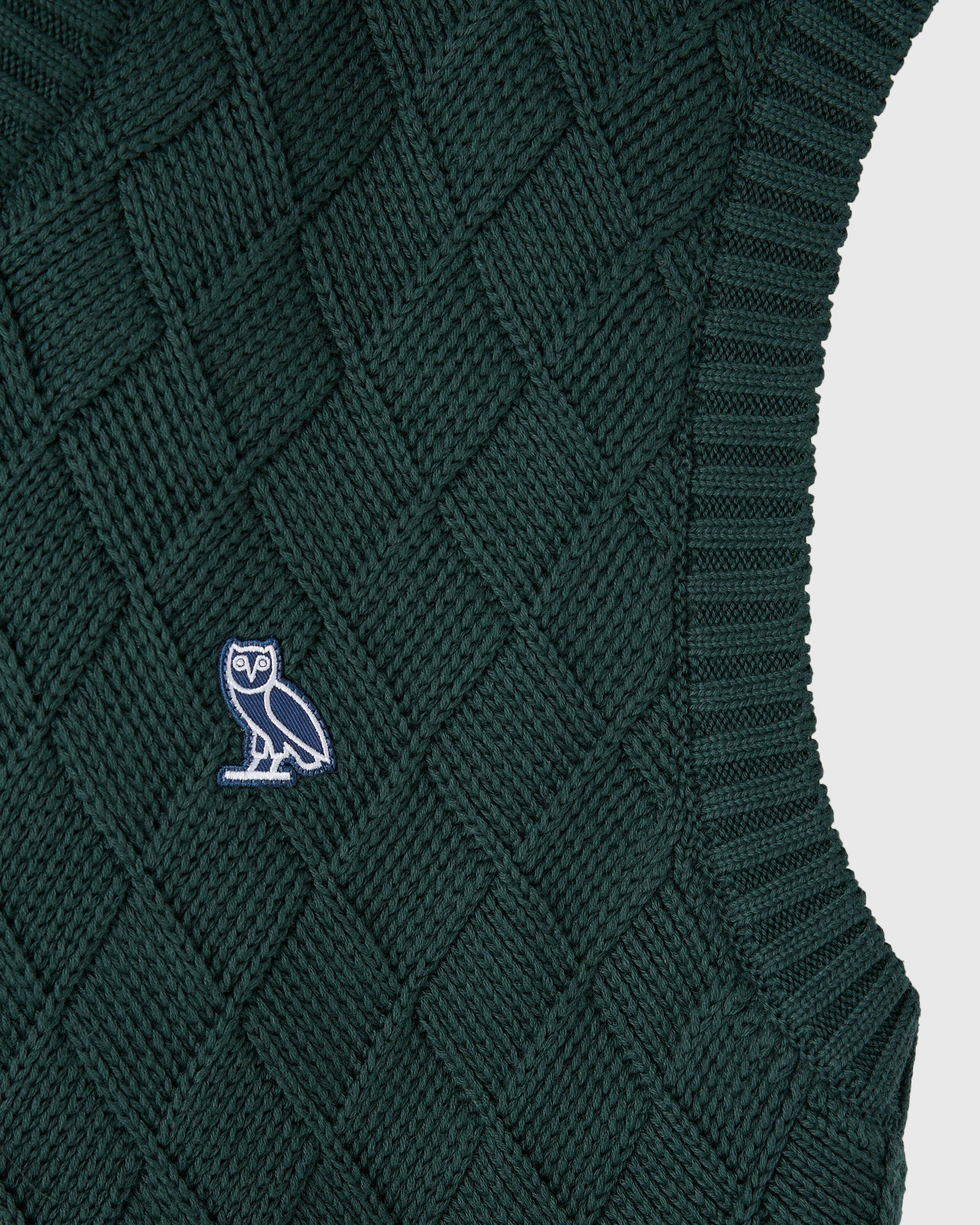 Midnight green basketweave knit sweater vest with small owl embroidered logo on chest and ribbed trim.
