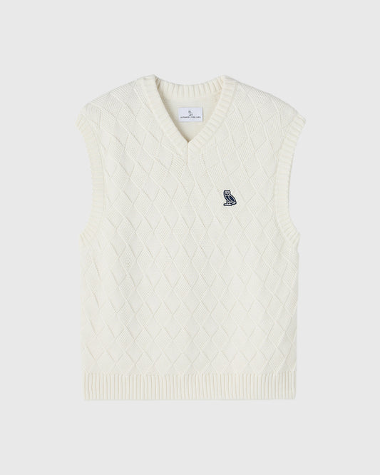 Cream-colored sleeveless sweater vest with basketweave knit pattern and small owl embroidery on chest.