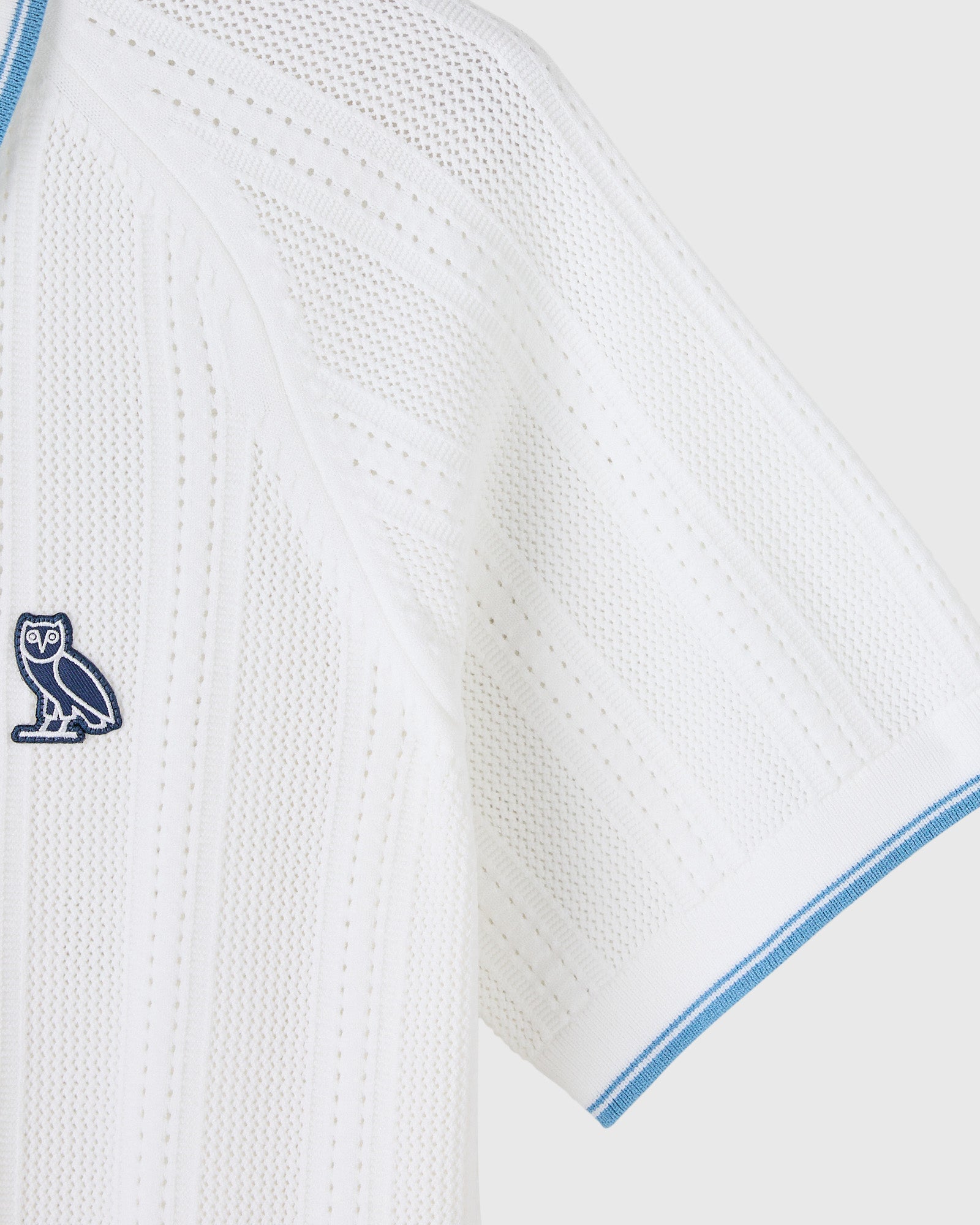 White open knit polo sweater with blue trim detailing and embroidered owl logo on chest.