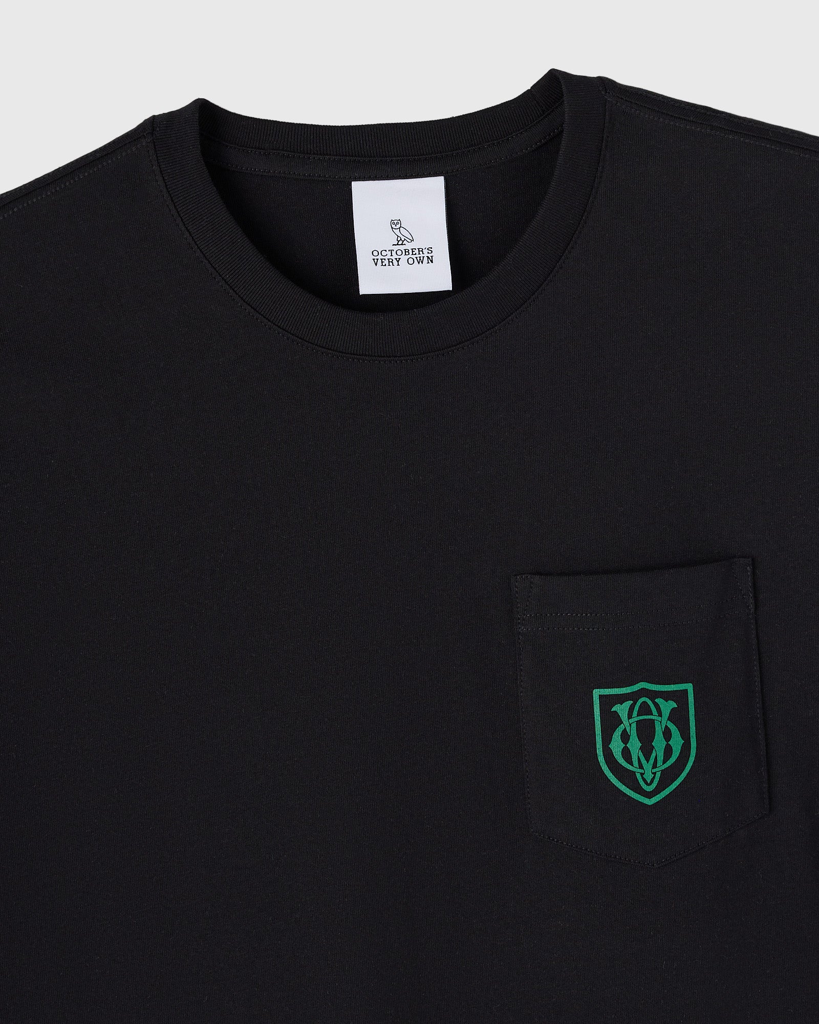 Black t-shirt with OVO owl crest logo in green on chest pocket and brand label at neckline.