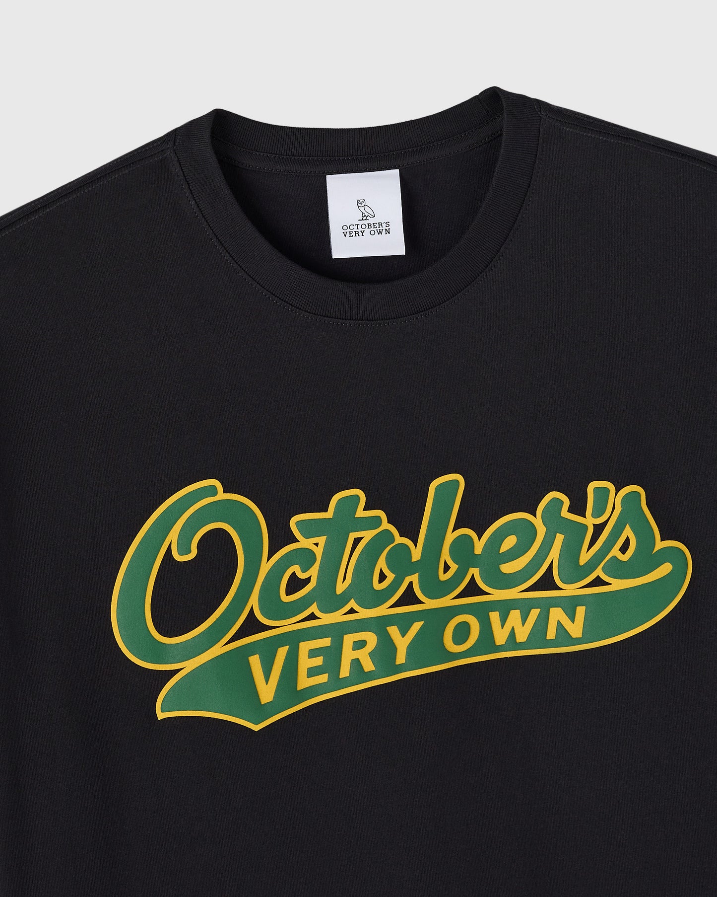 Black crewneck tee with yellow and green script text reading "Ostlers Very Own" across the chest.