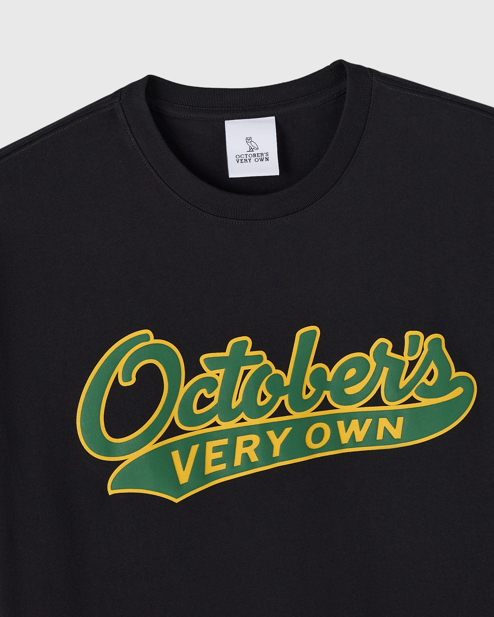 Black crewneck tee with yellow and green script text reading "Ostlers Very Own" across the chest.