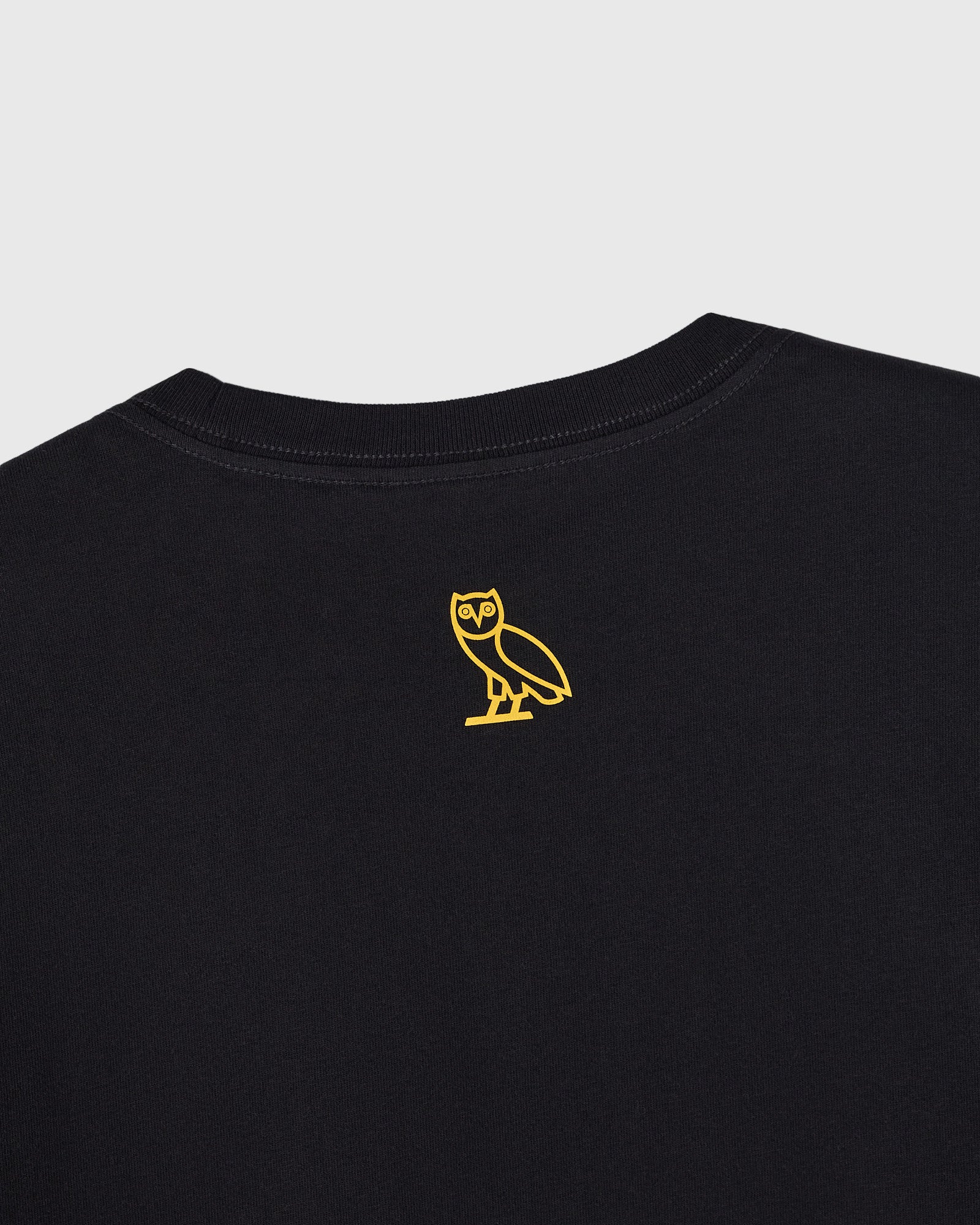 Black crewneck t-shirt with small yellow owl outline graphic on chest.