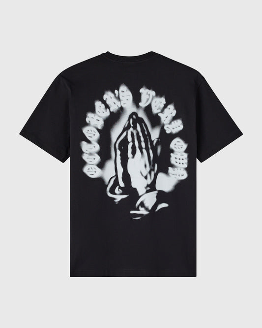 Black t-shirt with white airbrushed graphic of praying hands surrounded by smiley faces on chest.