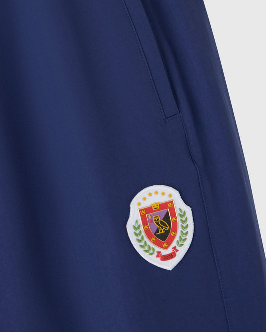 Deep denim nylon trackpant with embroidered crest patch on thigh.