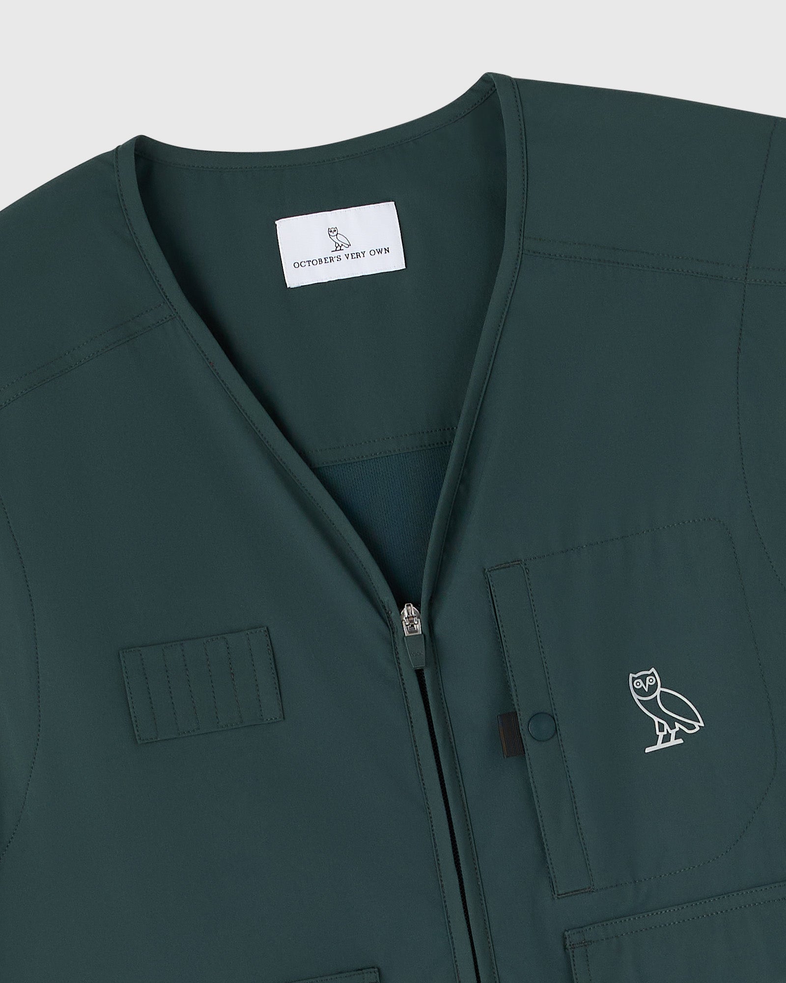Midnight green stretch nylon golf vest with front zip closure, chest pockets, and OVO owl logo embroidered on chest.
