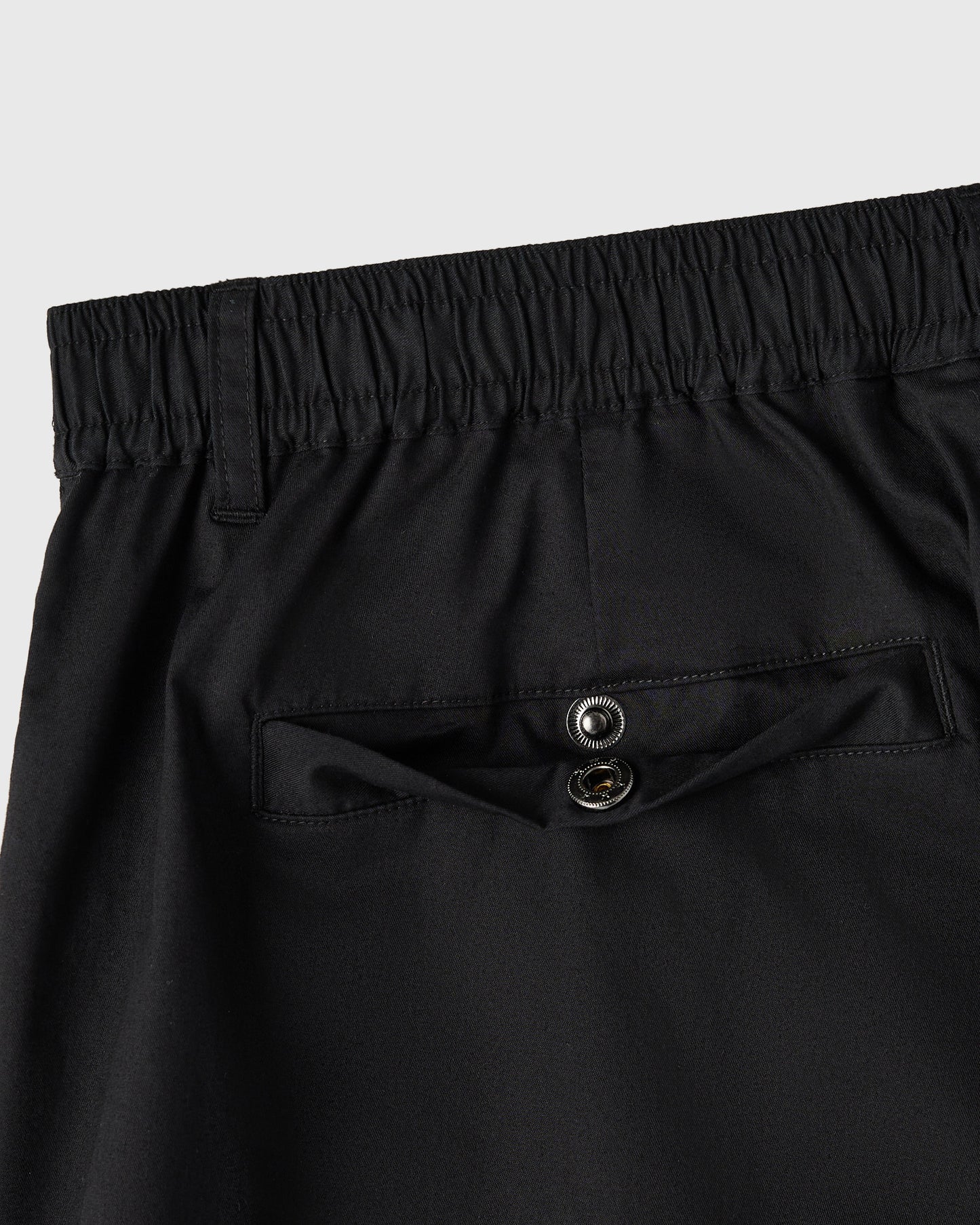 Black camp short with elastic waistband, metal button details on chest pocket, and stitched seams.