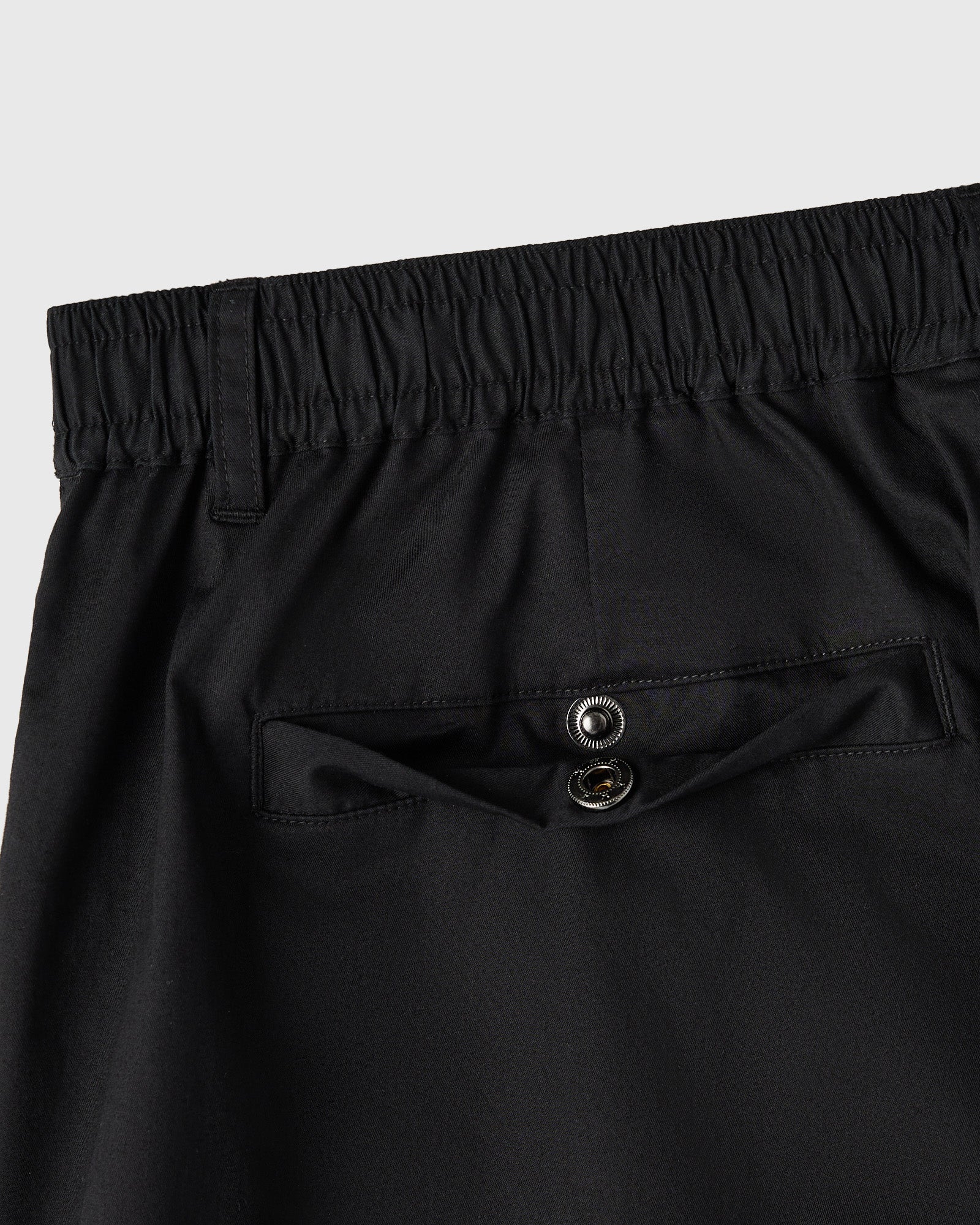 Black camp short with elastic waistband, metal button details on chest pocket, and stitched seams.